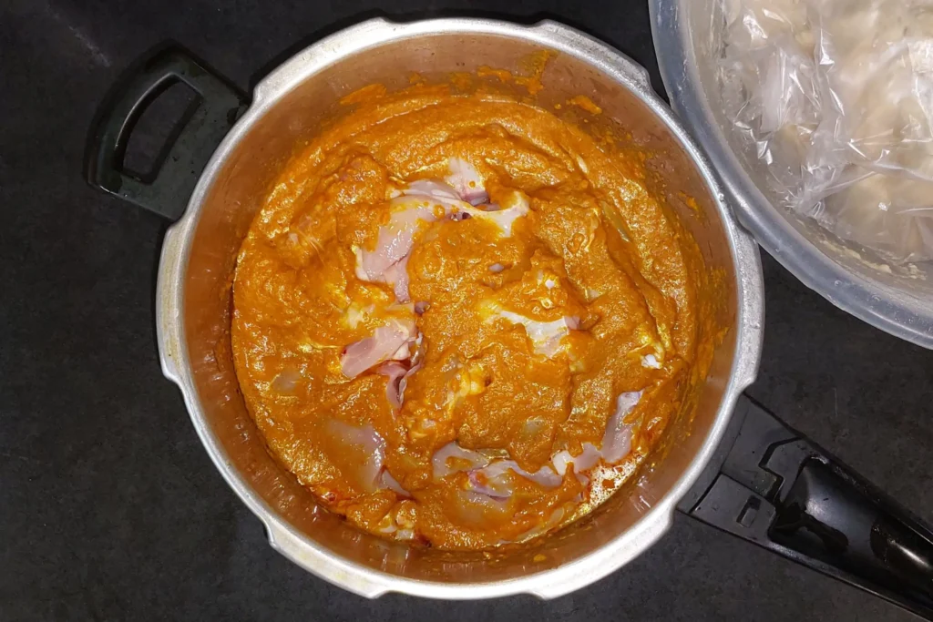 Dumping chicken into the pot with the masala