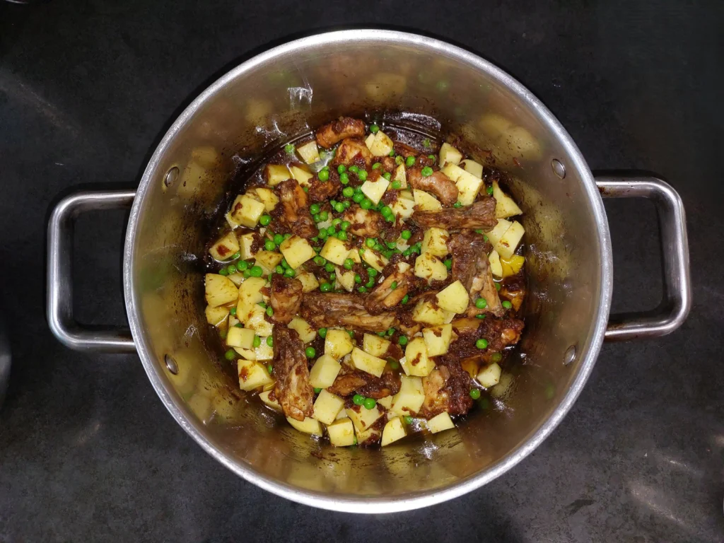 Adding potatoes and peas to the chicken and onions
